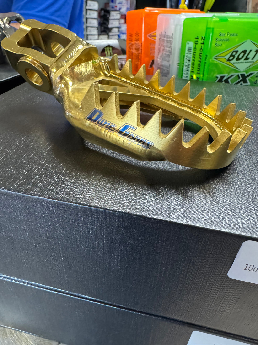 Dune Goons titanium foot pegs in gold anodized finish for Stark Varg, side view with Dune Goons logo
